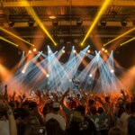 Energetic music concert scene with bright lights and a lively cheering crowd indoors.